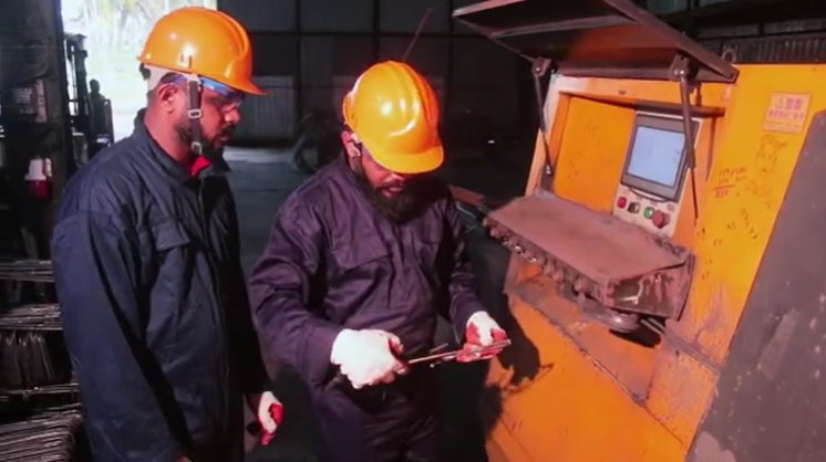 Two workers inspecting a bent stirrup at the CNC bending machine